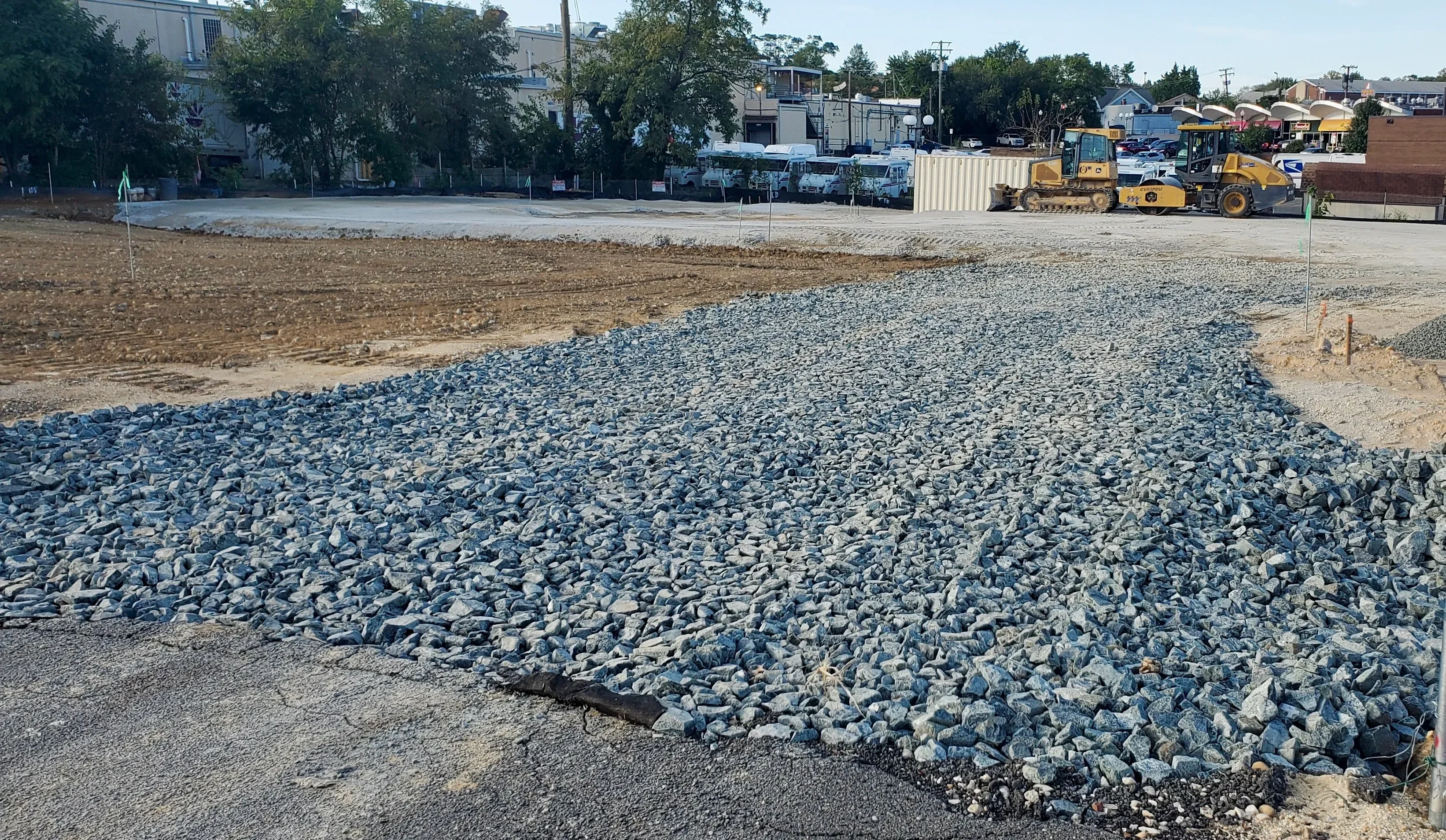 A stabilized gravel construction entrance pad installed at a Charlotte, NC job site with seed straw applied to surrounding disturbed soil. Truck tire tracks are visible across the gravel pad leading from the site access point to the adjacent road.
