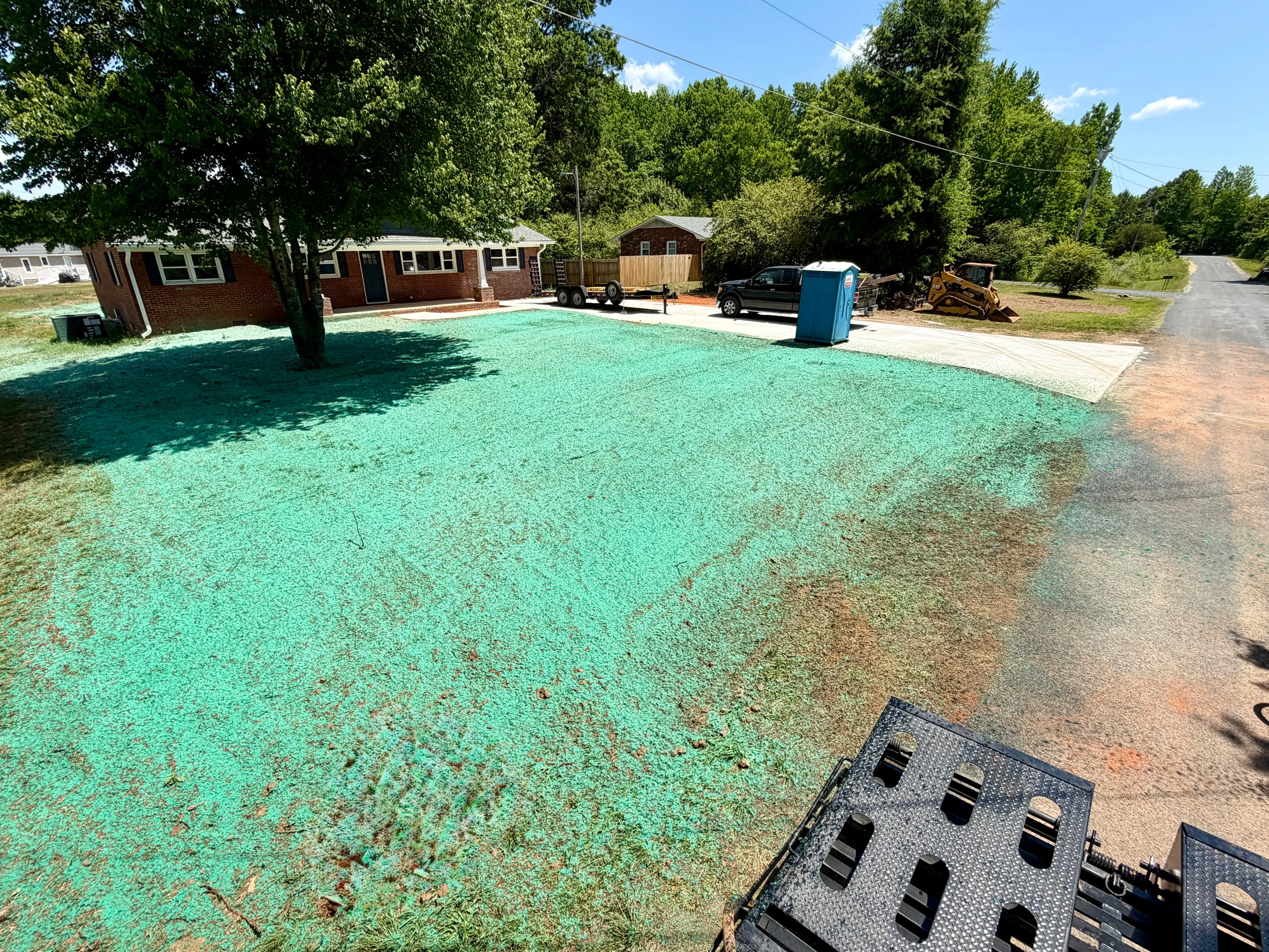 A freshly hydroseeded residential slope in Charlotte, NC with a bright green slurry coating covering bare red clay soil. A graded yard extends behind the treated area, showing the scale of a typical post-construction hydroseeding application.