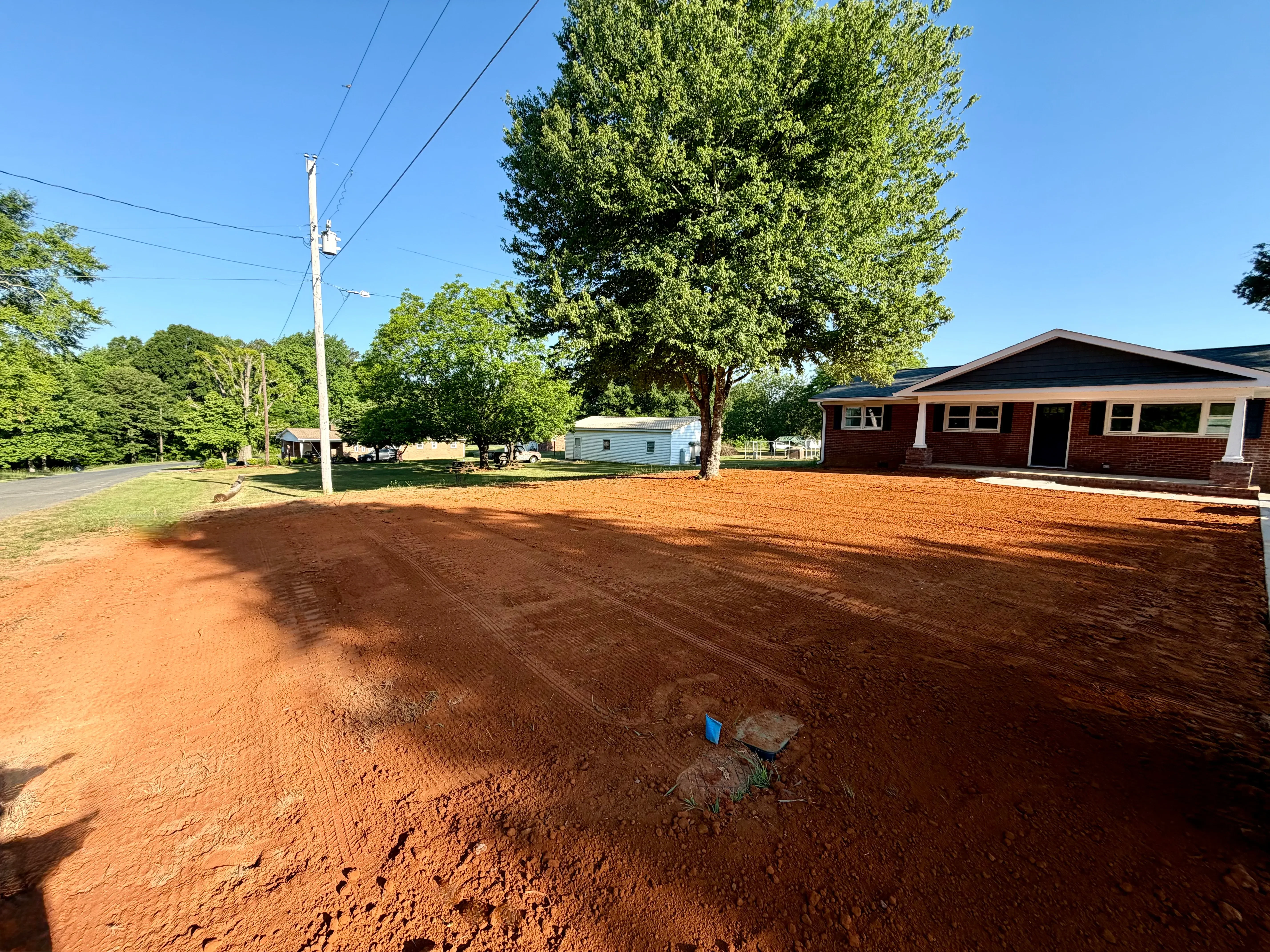 A freshly tilled and graded soil surface on a residential slope in Charlotte, NC, prepared for seeding with visible amendment work and smooth drainage contours. Red clay subsoil has been broken up and leveled in preparation for erosion control seeding by Terra Set.